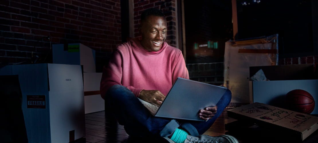 man using laptop on floor around moving boxes